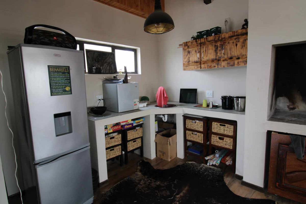 A rustic kitchenette area featuring built-in concrete counters, a corner sink, wooden wall-mounted cabinets, and an integrated fireplace.