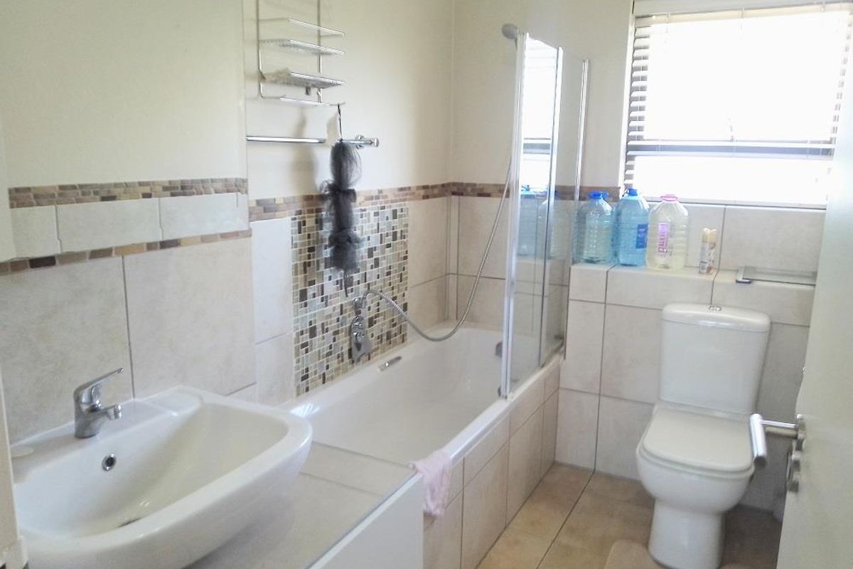 A functional bathroom featuring a bathtub with a glass shower screen, a pedestal basin, and a toilet, finished with neutral wall and floor tiles.