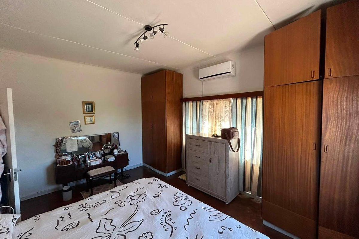 A bedroom featuring built-in wooden cupboards, a split-system air conditioning unit, and a ceiling light fixture.