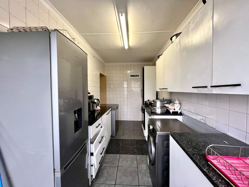 A functional galley-style kitchen featuring white cabinetry, dark granite countertops, tiled backsplash, and tiled flooring with integrated appliance spaces.