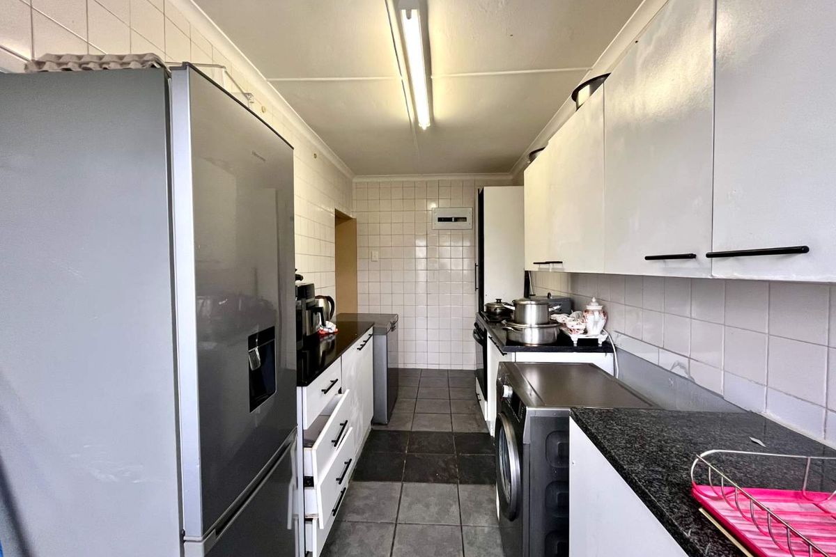 A functional galley-style kitchen featuring white cabinetry, dark granite countertops, tiled backsplash, and tiled flooring with integrated appliance spaces.