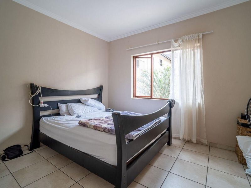 A functional bedroom featuring tiled flooring, neutral wall tones, and a timber-framed window allowing natural light.