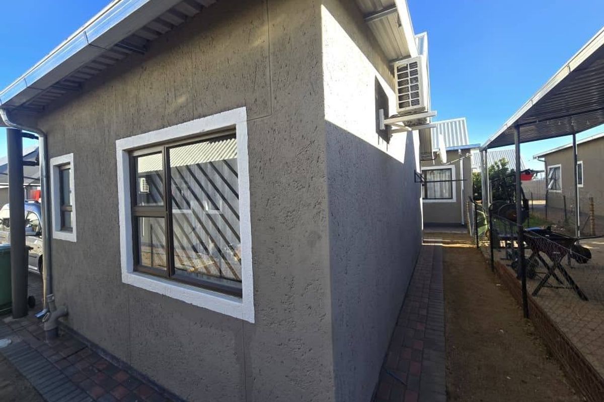 Side exterior view of the townhouse featuring textured plaster walls, aluminium window frames with security bars, and a wall-mounted air conditioning unit.