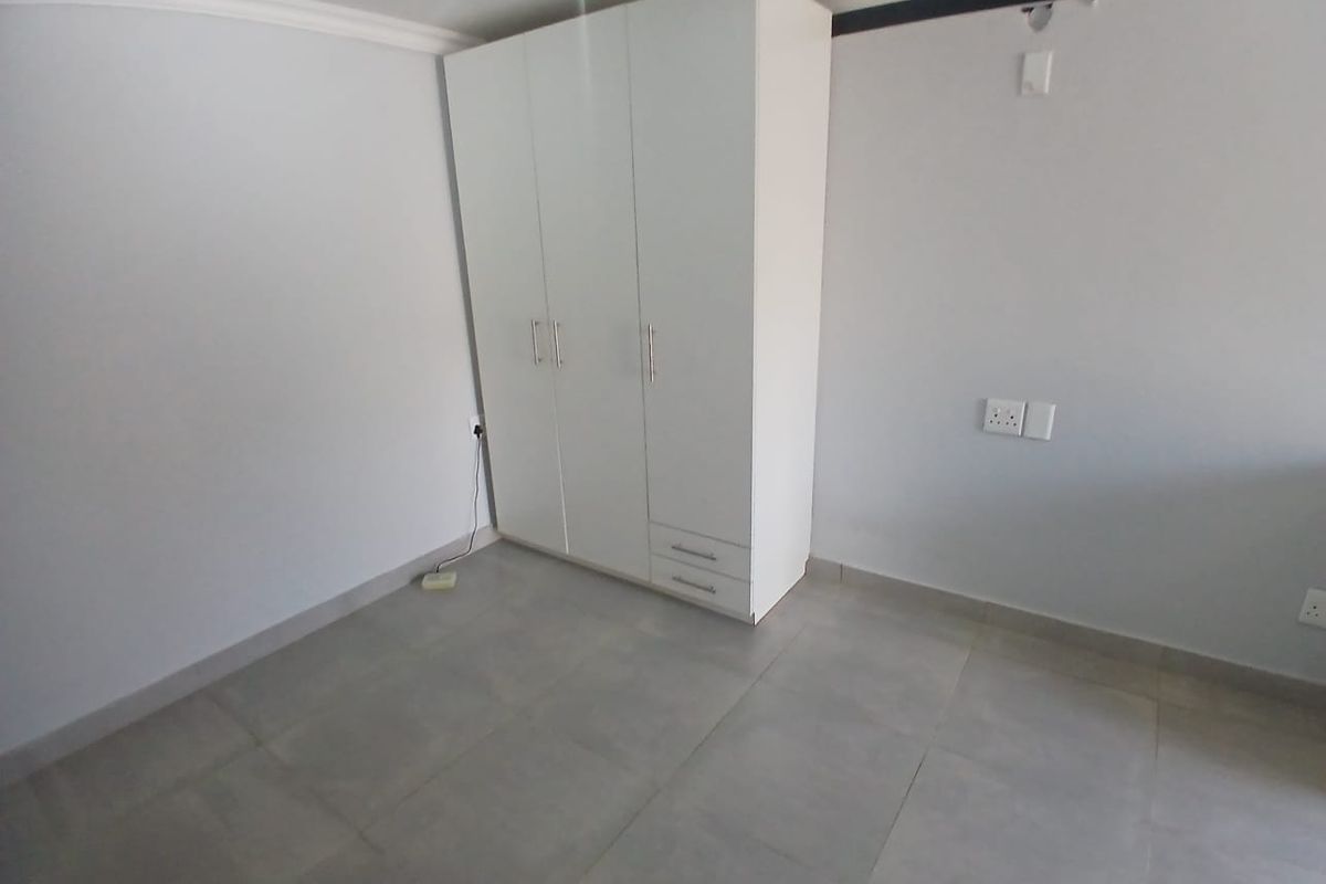 A clean, empty bedroom featuring neutral tiled flooring and a built-in white wardrobe, providing a versatile space ready for personalization.