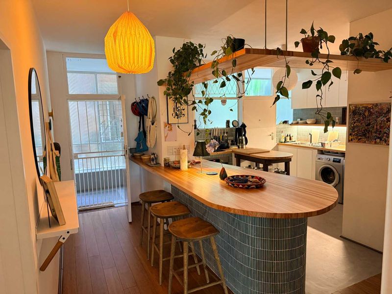Open plan kitchen area featuring a curved breakfast bar, tiled backsplash, integrated laundry appliance, and timber shelving with modern finishes.