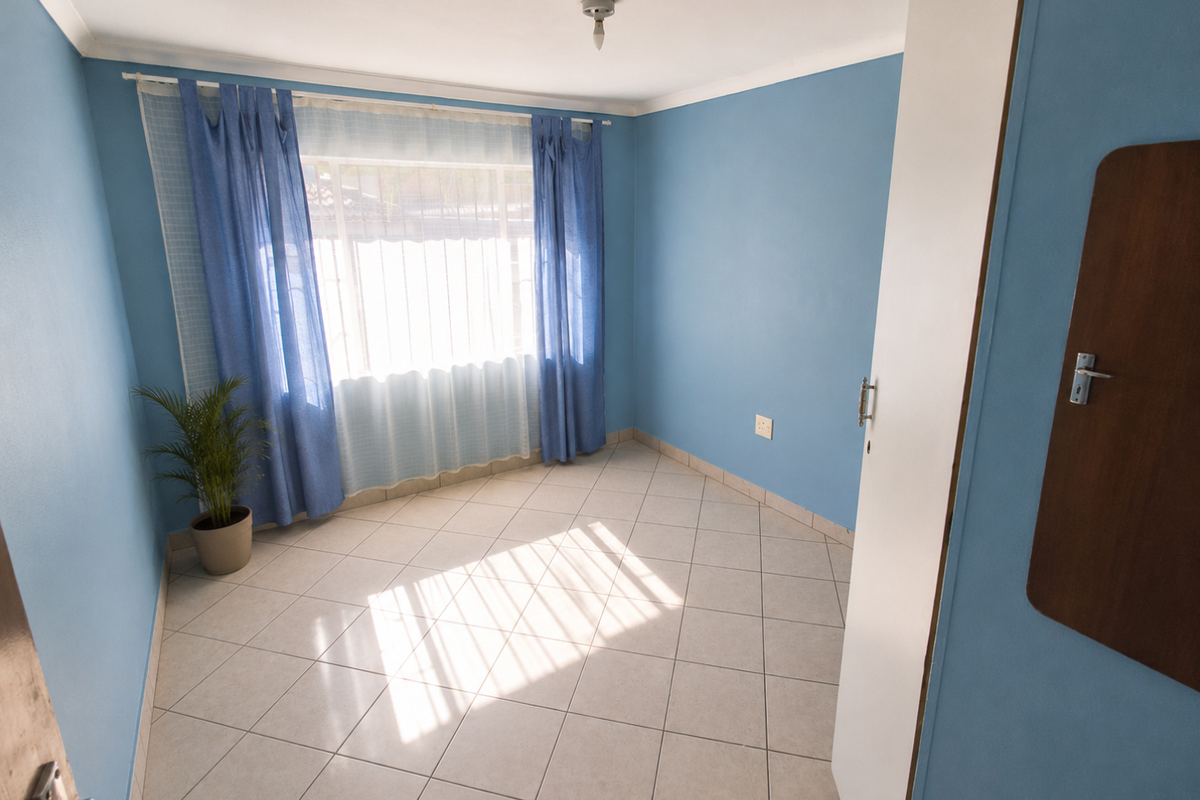 A bright, empty bedroom featuring light-colored floor tiles, blue painted walls, and a window with curtains.