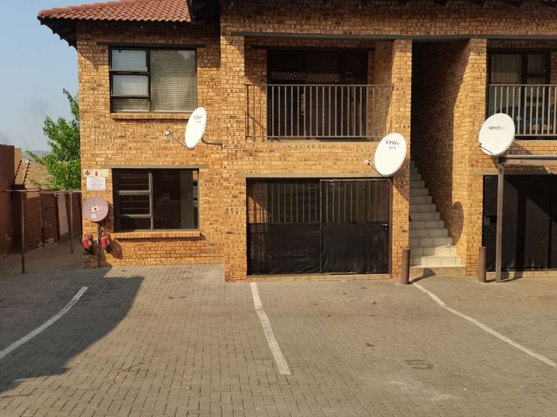 Front elevation of a face-brick apartment complex featuring a paved driveway, balcony access, and secure metal gates.