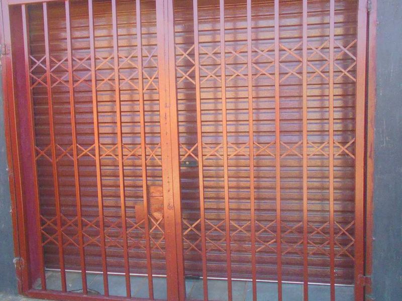A secure entrance featuring a double-panel metal security gate over a solid wooden door, providing robust exterior access protection.