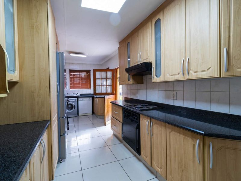 Functional kitchen featuring light wood cabinetry, dark granite countertops, built-in oven and hob, tiled flooring, and a skylight for natural illumination.