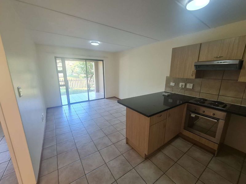 Open-plan kitchen and living area featuring tiled floors, built-in cabinetry with granite countertops, and a sliding door leading to an outdoor patio space.