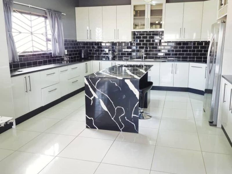 Modern kitchen featuring high-gloss white cabinetry, a striking black and white marble-look island, subway tile backsplash, and large format ceramic floor tiles.