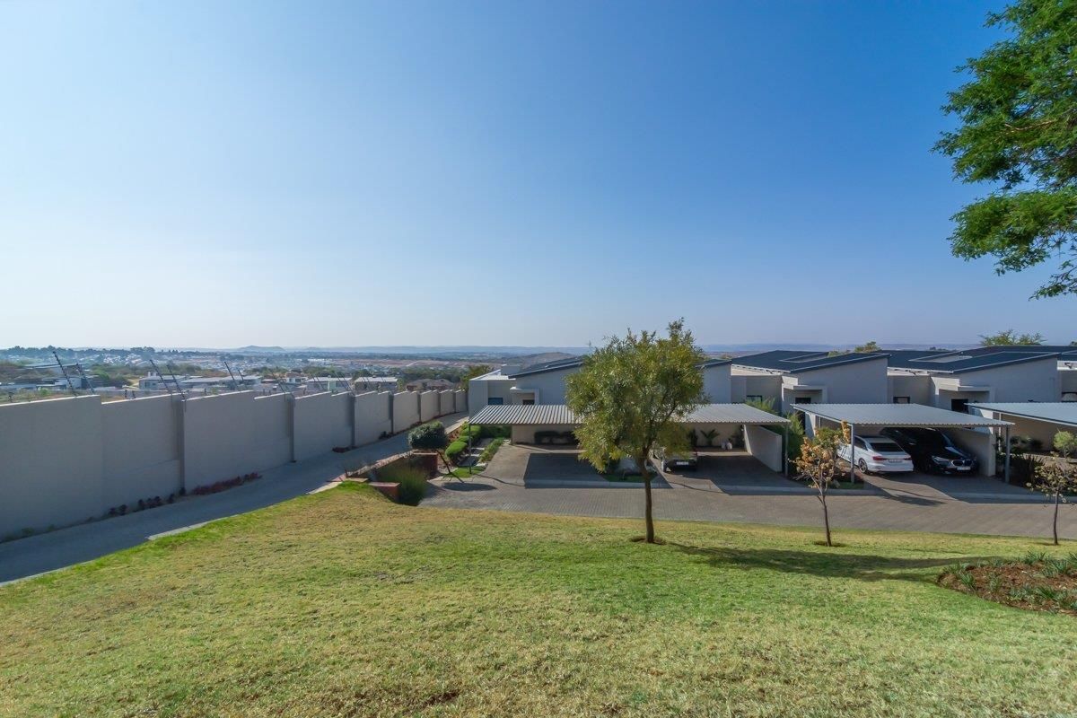 Elevated aerial view of a townhouse complex featuring paved driveways, covered carports, and perimeter security walling with electric fencing.