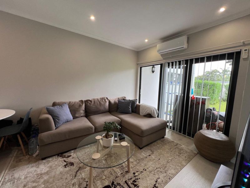A comfortable living room featuring recessed downlighting, a wall-mounted split-system air conditioner, and large sliding glass doors that provide access to the outdoor area.