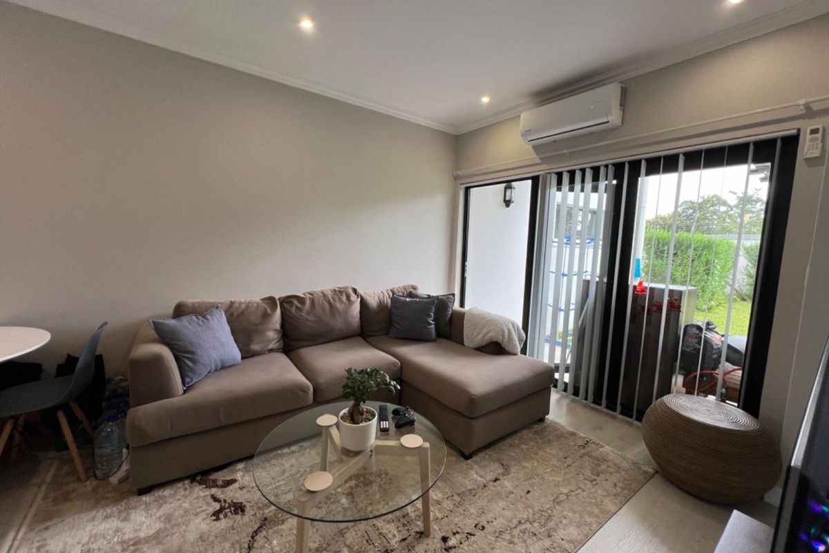 A comfortable living room featuring recessed downlighting, a wall-mounted split-system air conditioner, and large sliding glass doors that provide access to the outdoor area.