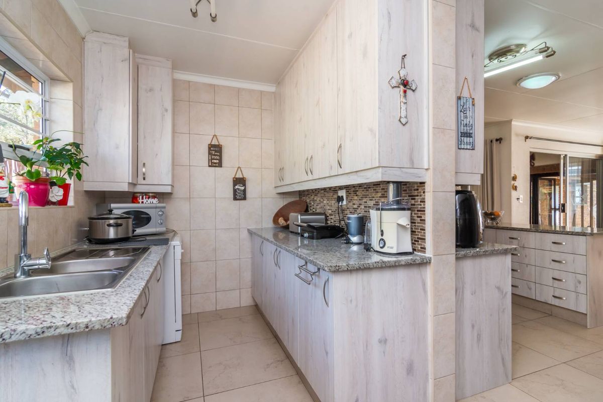 A functional kitchen featuring light-toned cabinetry, granite countertops, a tiled backsplash, and a stainless steel double sink with a view into the adjacent living area.
