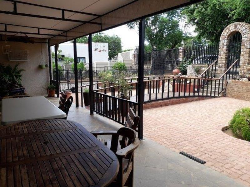 A spacious covered patio overlooking a paved courtyard with a decorative brick archway, metal railings, and a raised garden area.