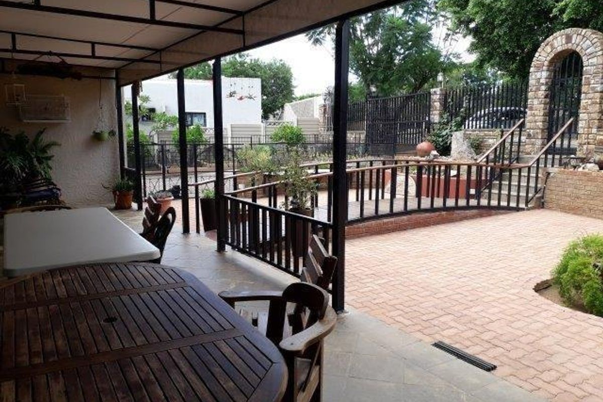 A spacious covered patio overlooking a paved courtyard with a decorative brick archway, metal railings, and a raised garden area.