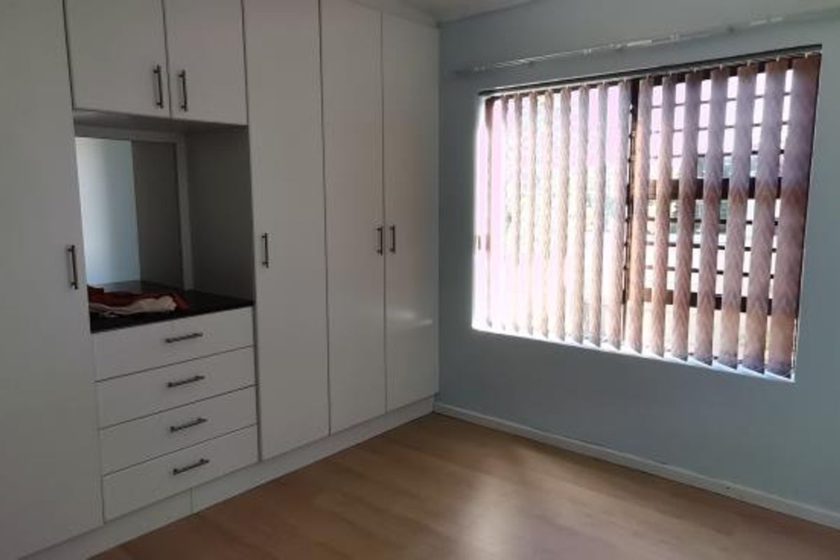 A bright bedroom featuring extensive built-in cabinetry with integrated vanity space, laminate flooring, and vertical window blinds.