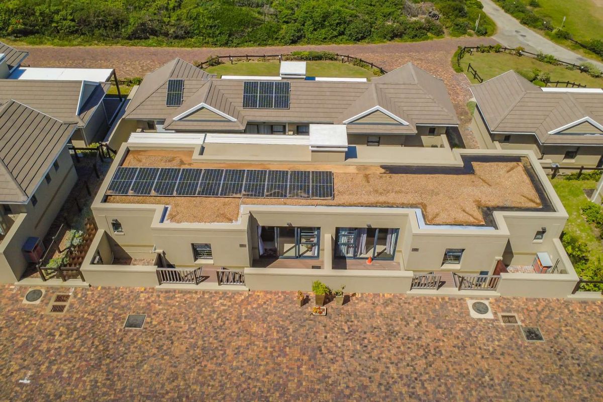 Aerial view of a townhouse complex featuring tiled pitched roofs, integrated solar panel arrays, and paved driveway access.
