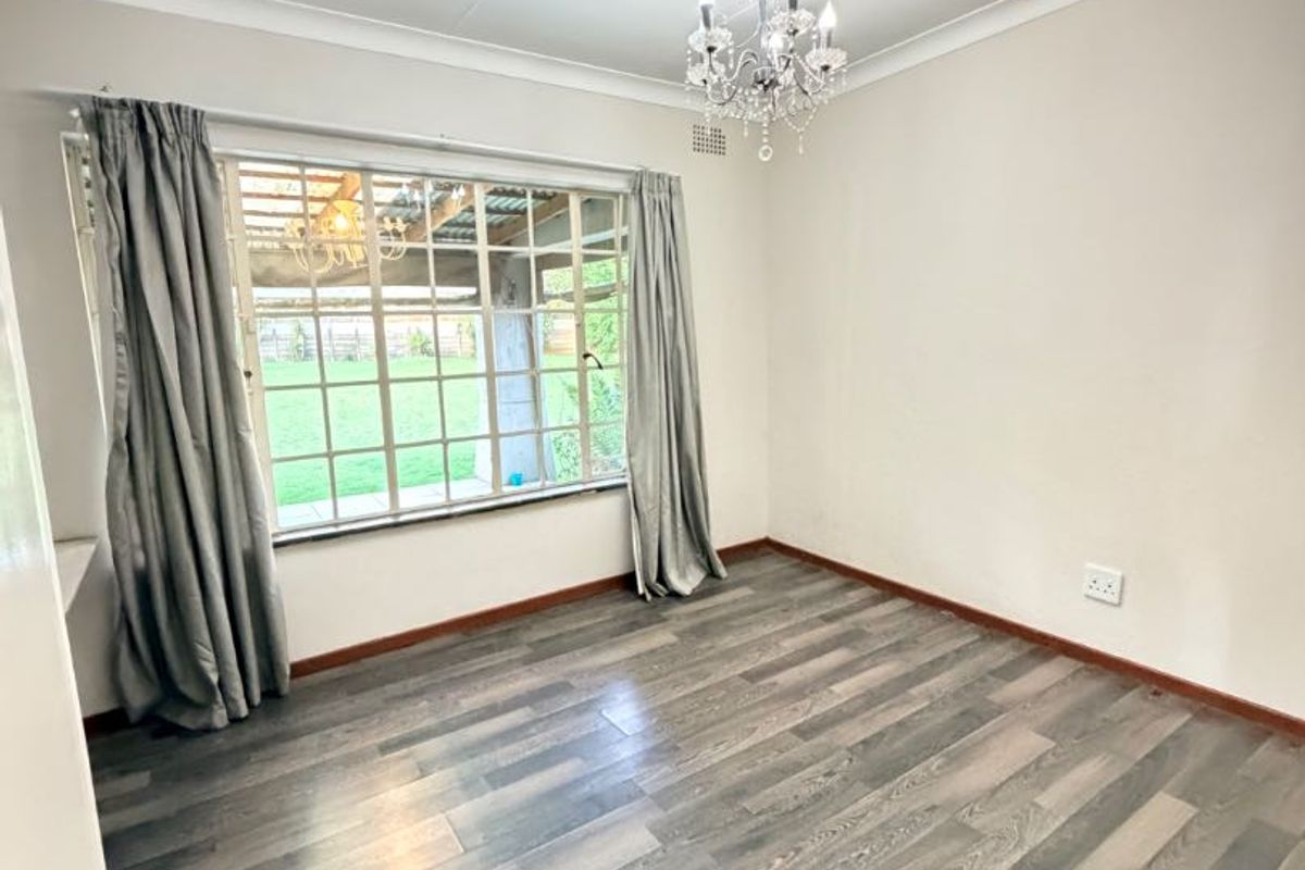 A bright, empty bedroom featuring modern grey laminate flooring, a coved ceiling, and a large multi-pane window overlooking the garden.