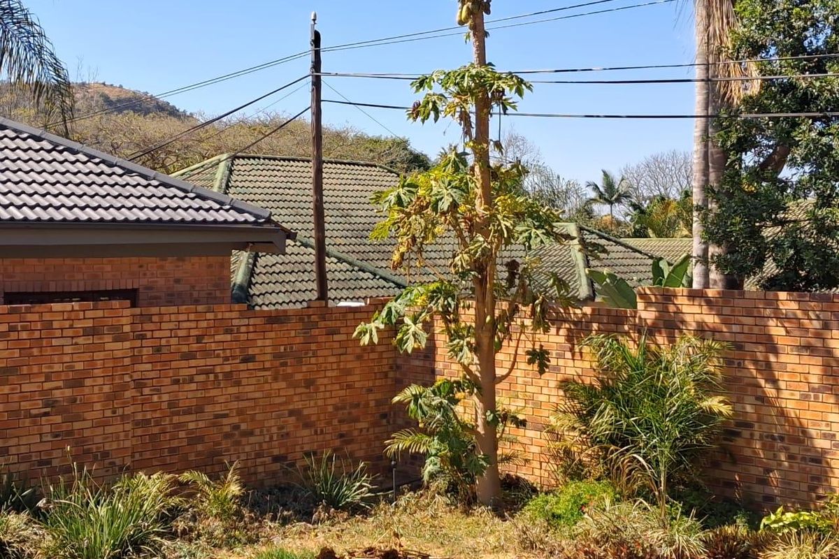 A view of the rear garden area featuring a brick boundary wall, tiled roof sections, and established landscaping.