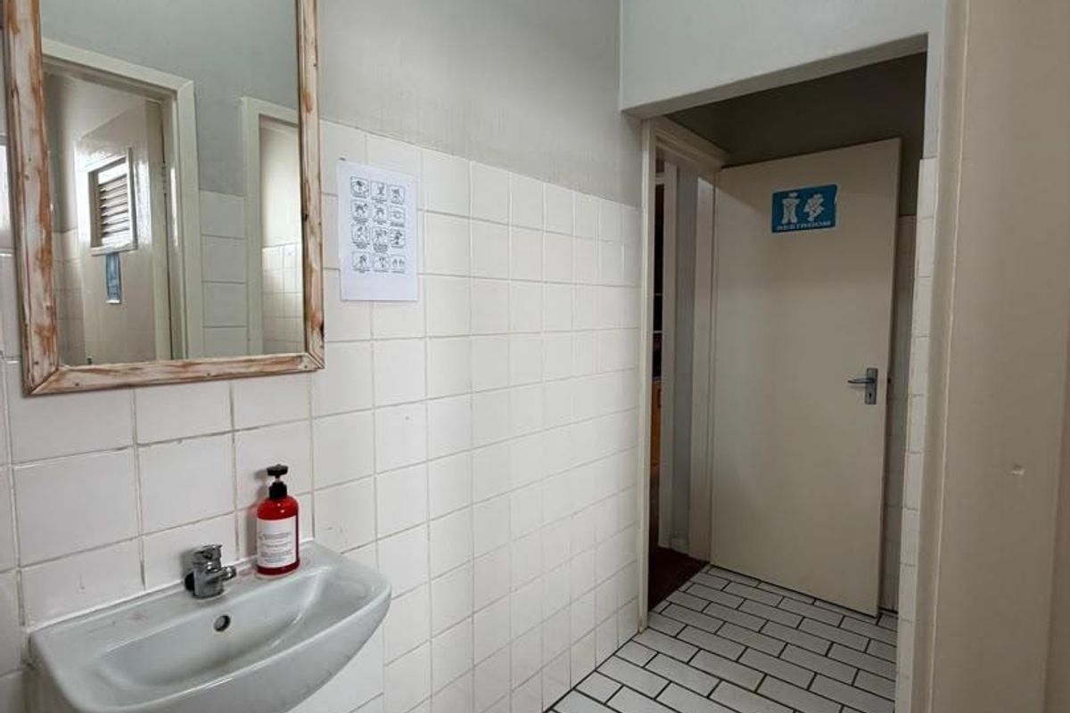 A functional office restroom area featuring a wall-mounted basin, tiled splashback, and tiled flooring, providing basic sanitary facilities for the workspace.