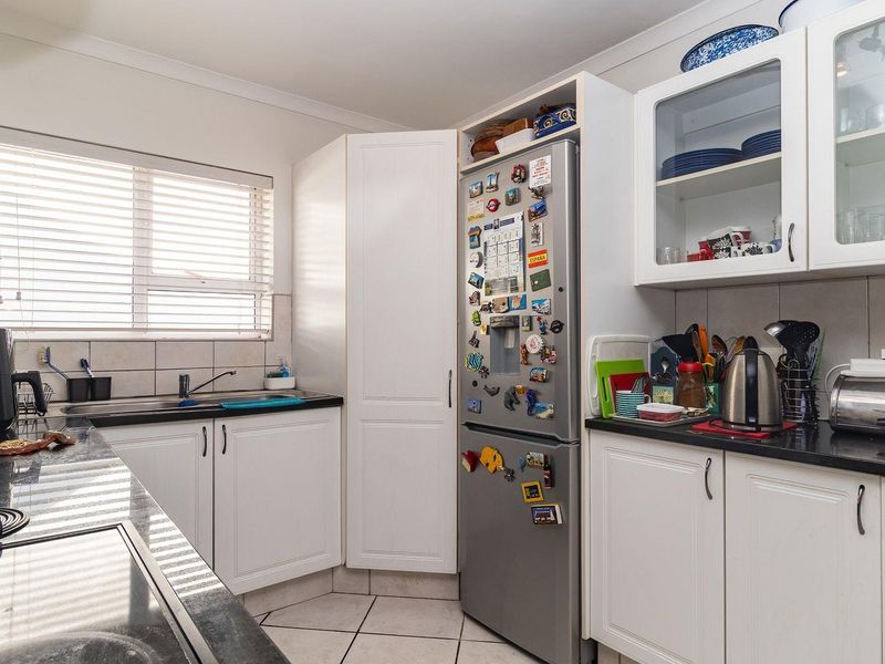 A functional kitchen featuring white cabinetry, dark laminate countertops, tiled backsplash, and ceramic floor tiles with a window providing natural light.