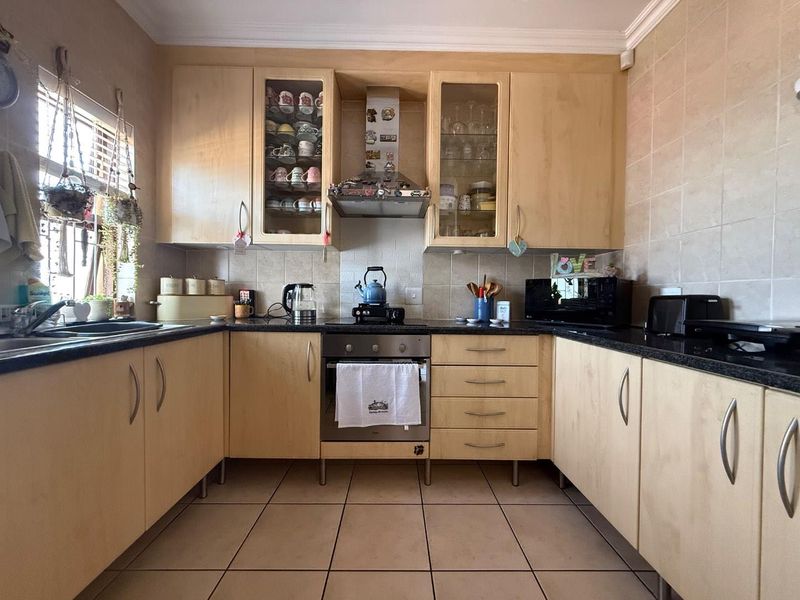 A functional U-shaped kitchen featuring light wood cabinetry, granite countertops, a built-in oven with extractor fan, and tiled flooring.