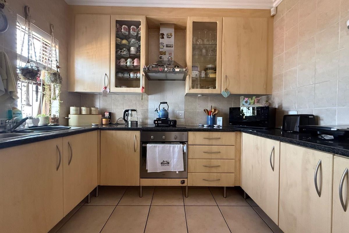 A functional U-shaped kitchen featuring light wood cabinetry, granite countertops, a built-in oven with extractor fan, and tiled flooring.