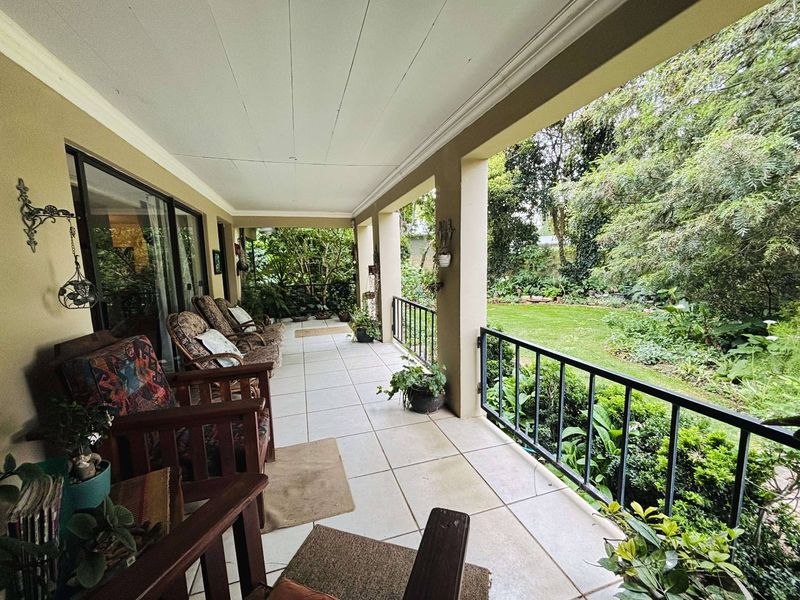 A spacious covered patio featuring tiled flooring and a metal balustrade, overlooking a lush, well-maintained garden area.
