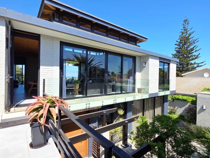 Modern multi-level rear exterior featuring a spacious tiled balcony with glass balustrades, large sliding doors, and a timber pergola overlooking the garden.