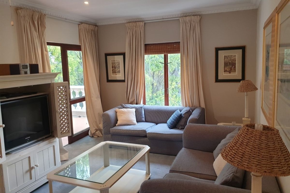 A comfortable living room featuring neutral wall tones, recessed ceiling lighting, and direct access to an outdoor balcony through glass-paneled doors.
