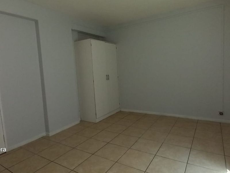 A simple, empty bedroom featuring neutral tiled flooring and a built-in cupboard, offering a clean canvas for personalization.