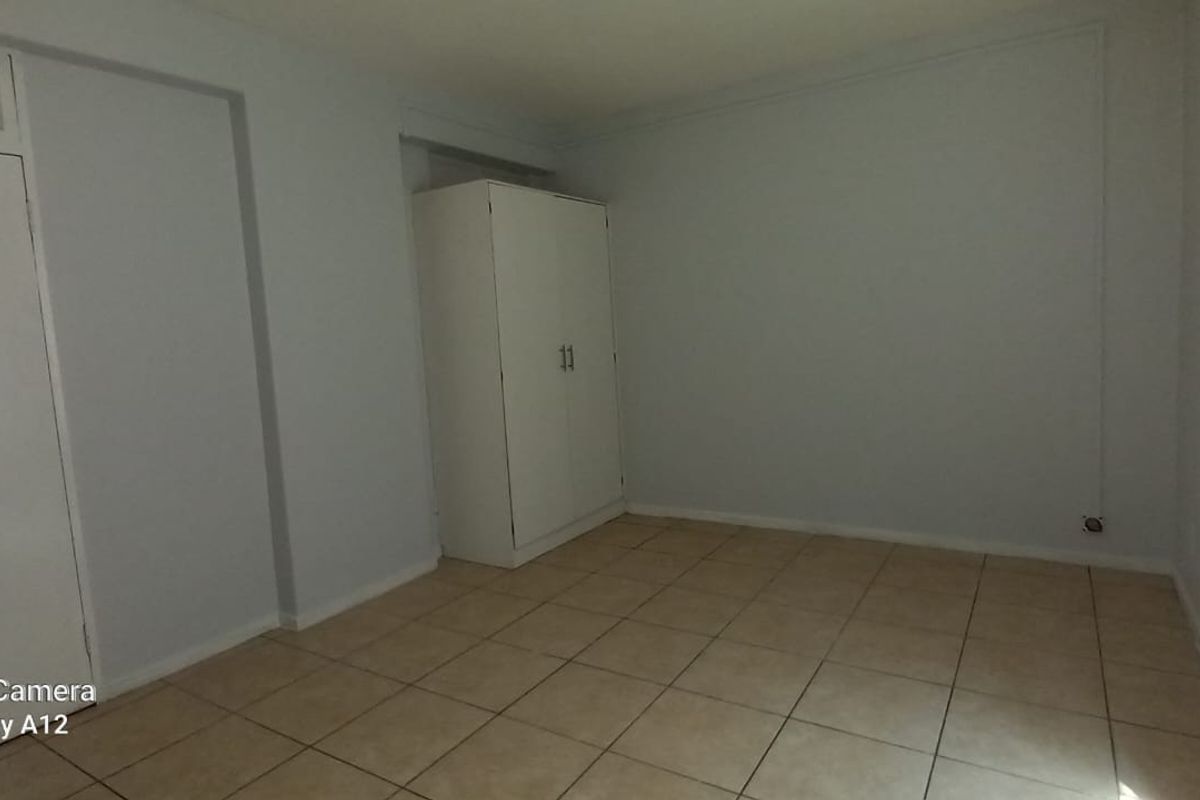 A simple, empty bedroom featuring neutral tiled flooring and a built-in cupboard, offering a clean canvas for personalization.