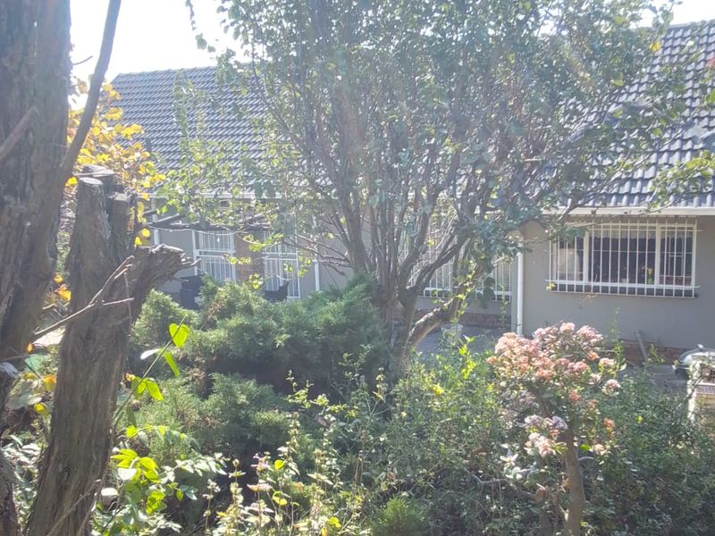 A view of the rear garden and house exterior, featuring a tiled roof, security bars on windows, and a stone pathway.