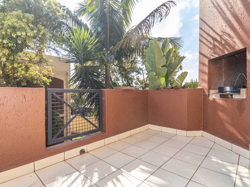 A private balcony featuring tiled flooring, a built-in braai, and a secure metal gate, offering a functional outdoor space for relaxation.