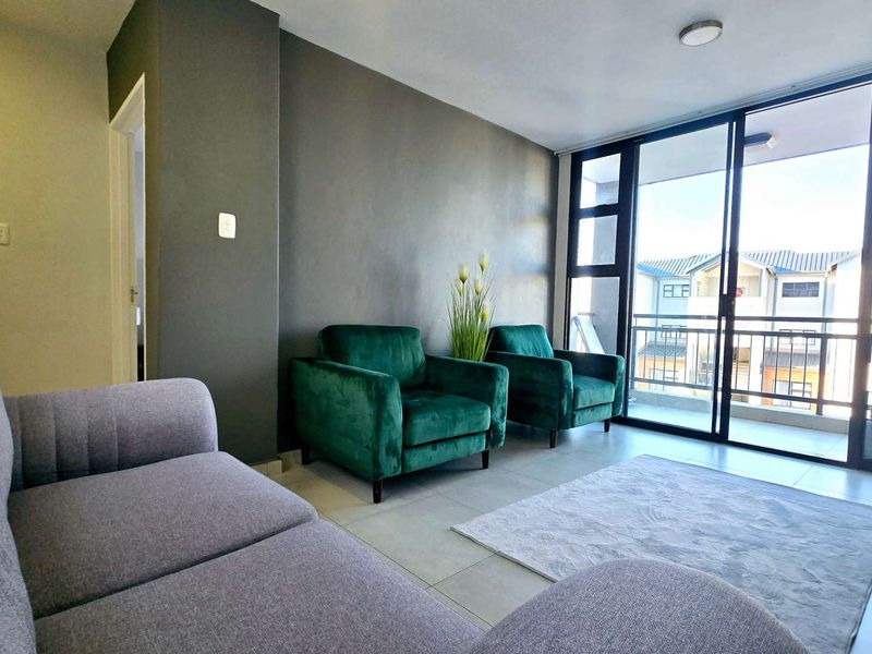 A bright living room featuring large sliding glass doors that open onto a balcony, with neutral tiled flooring and a modern accent wall.