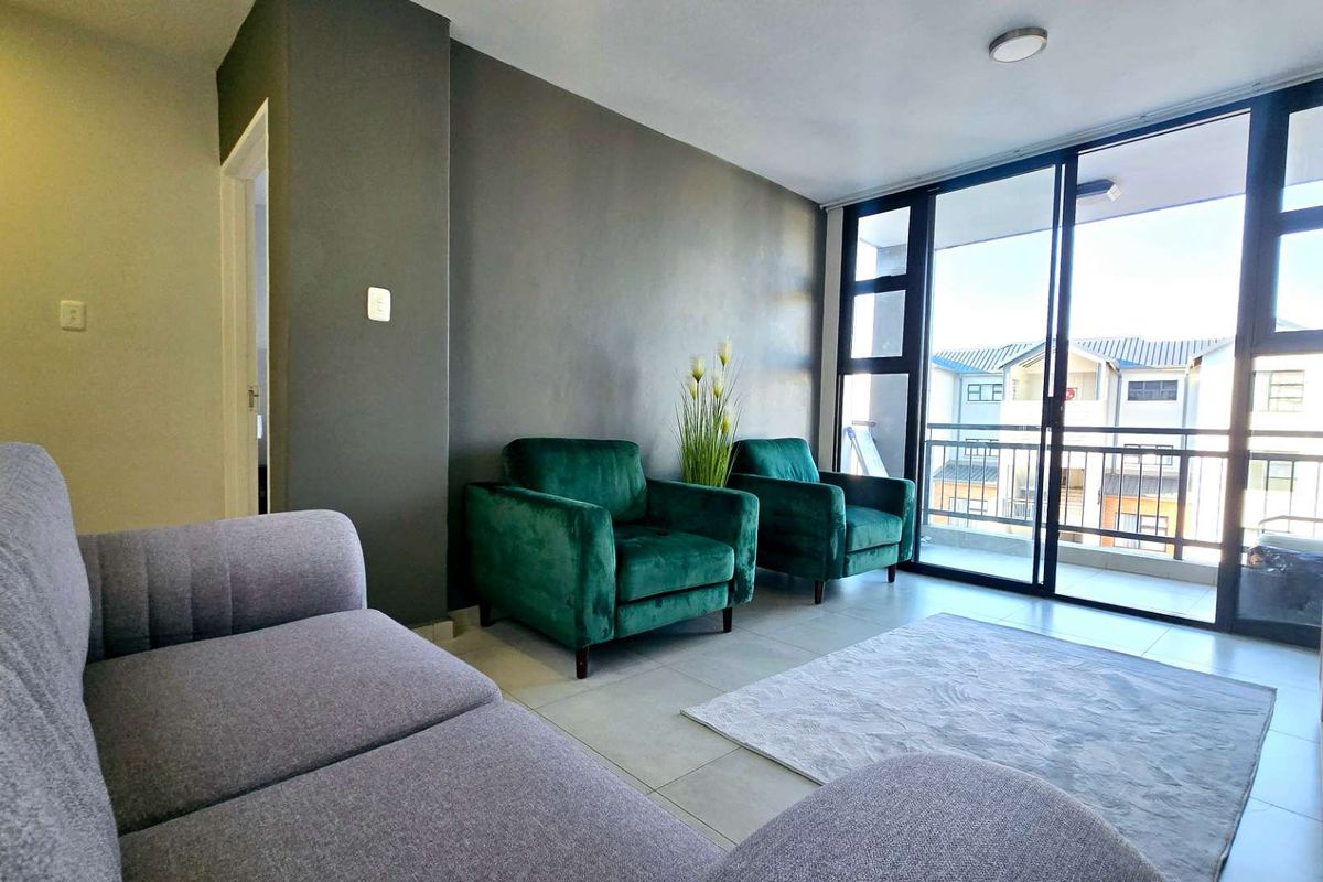 A bright living room featuring large sliding glass doors that open onto a balcony, with neutral tiled flooring and a modern accent wall.