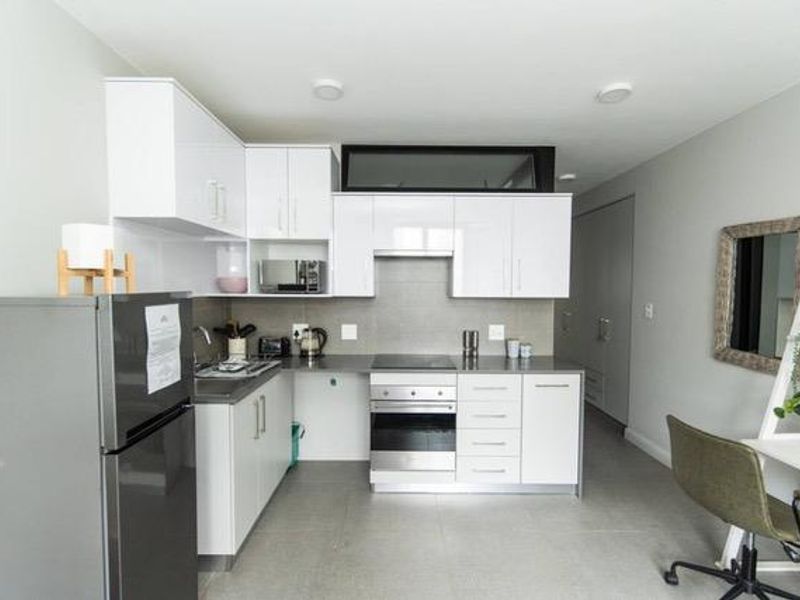 Modern kitchen featuring white high-gloss cabinetry, integrated oven and hob, stainless steel sink, and neutral tiled flooring in an open-plan layout.