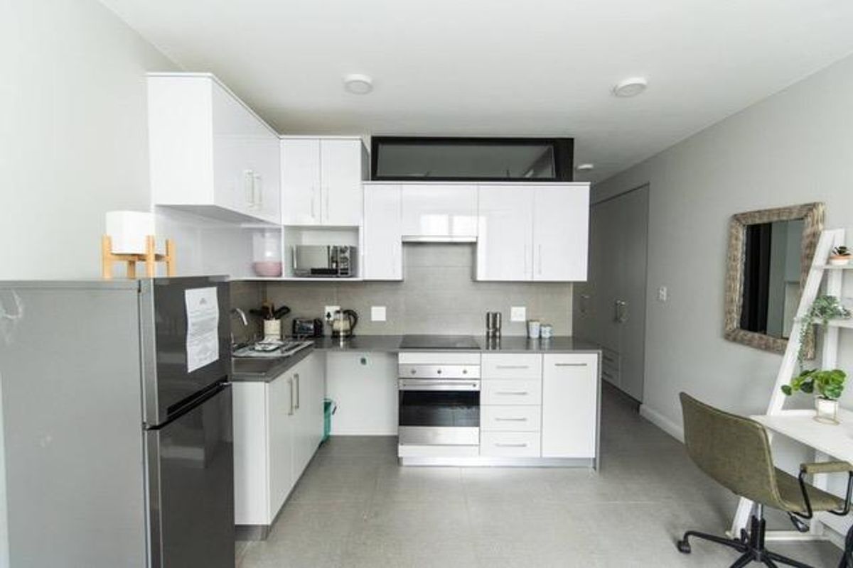 Modern kitchen featuring white high-gloss cabinetry, integrated oven and hob, stainless steel sink, and neutral tiled flooring in an open-plan layout.