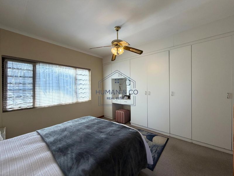 A bedroom featuring extensive built-in white cabinetry with an integrated vanity station and a ceiling fan.