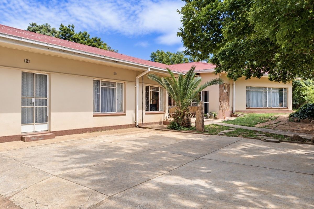 Rear view of the property featuring a large concrete paved area, established garden, and traditional single-story building structure with a metal roof.