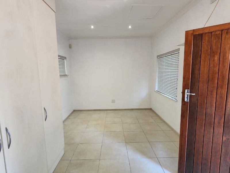 A clean, empty bedroom featuring neutral tiled flooring, built-in cupboards, and venetian blinds, offering a versatile space ready for personalization.