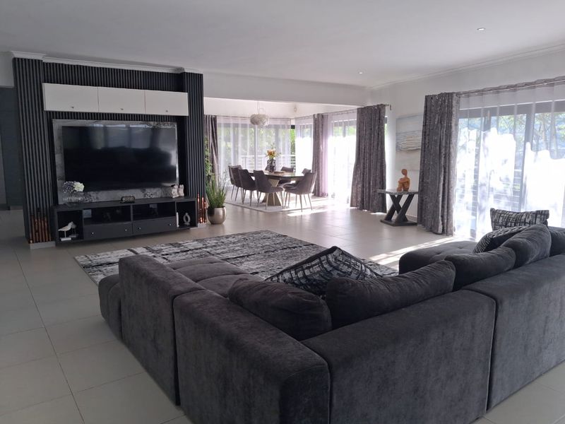 Spacious open-plan living and dining area featuring a modern built-in media wall, large format floor tiles, and abundant natural light through sliding glass doors.