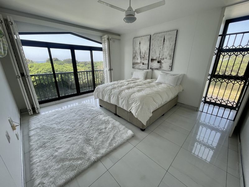 A bright bedroom featuring polished tiled floors, a ceiling fan, and large sliding glass doors that open onto a balcony with scenic views.