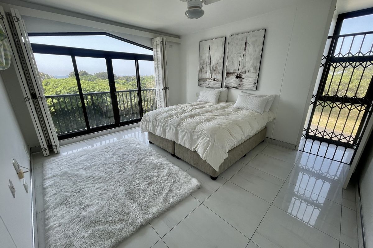 A bright bedroom featuring polished tiled floors, a ceiling fan, and large sliding glass doors that open onto a balcony with scenic views.