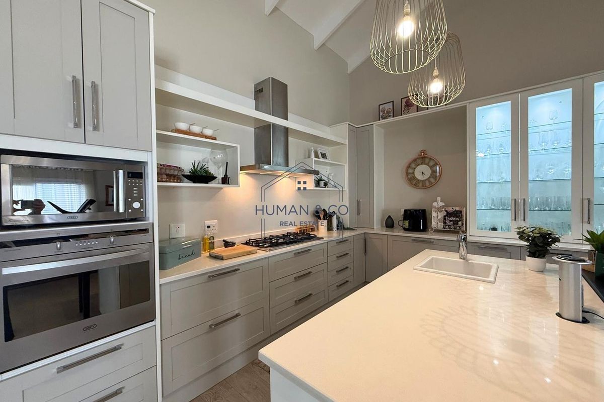 Modern kitchen featuring light grey cabinetry, stone countertops, a central island with a sink, built-in oven, microwave, and high vaulted ceilings.
