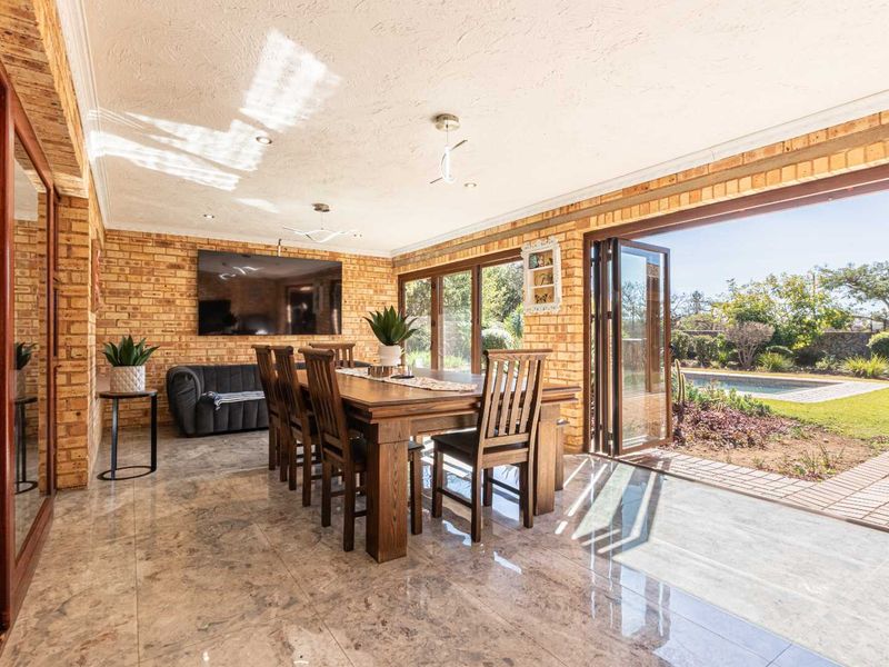 Spacious open-plan living and dining area featuring exposed brick walls, polished marble flooring, and seamless bi-fold doors opening to the pool and garden.