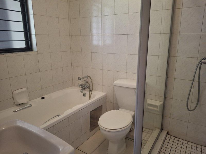 A functional bathroom featuring a bathtub, separate shower enclosure, and toilet with neutral wall and floor tiling.