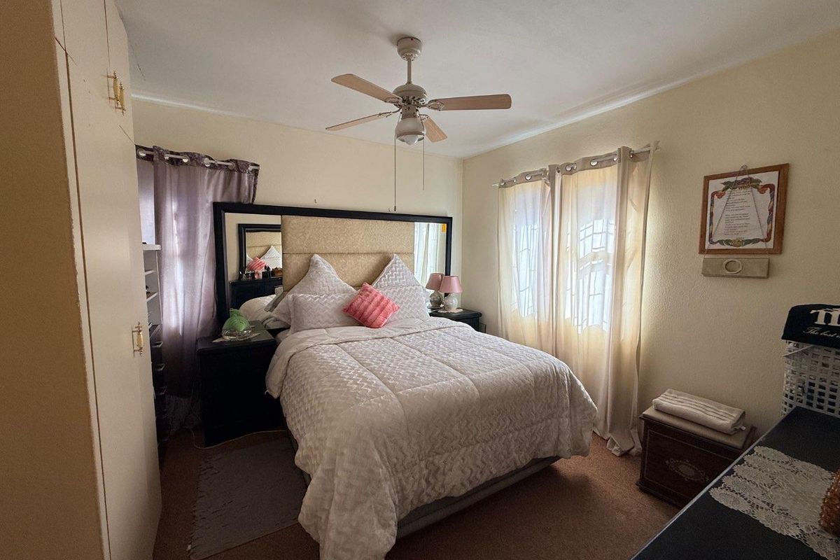 A cozy bedroom featuring built-in wardrobe cabinetry, a ceiling fan, and natural light through dual windows.